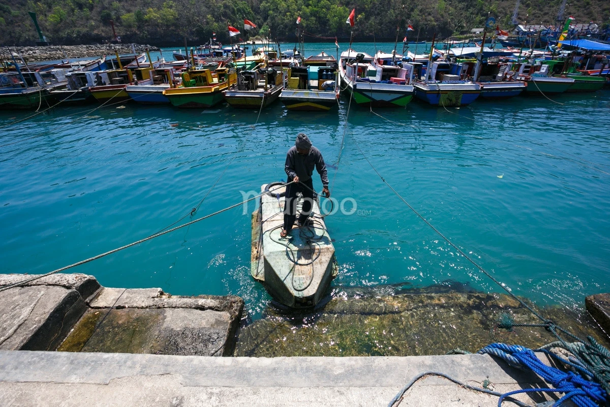 A fisherman secures a boat at a colorful port filled with fishing boats in a clear turquoise sea.