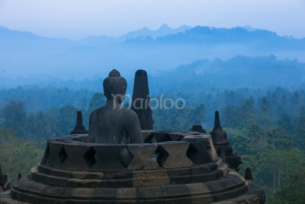 A Buddha statue inside a stupa at Borobudur Temple with a scenic view of surrounding hills.