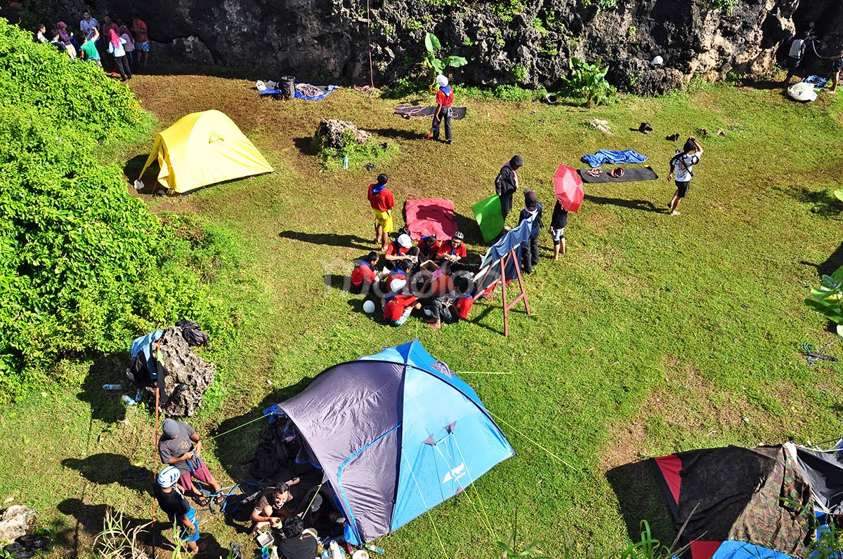 A group of people camping and preparing for rock climbing at Siung Beach, with colorful tents and gear.