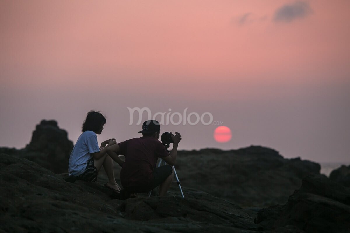 Two people capturing the sunset at Wediombo Beach, Yogyakarta.