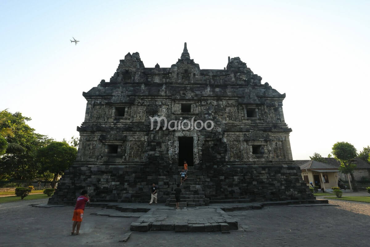 Children playing at the front of Sari Temple with an airplane flying overhead.