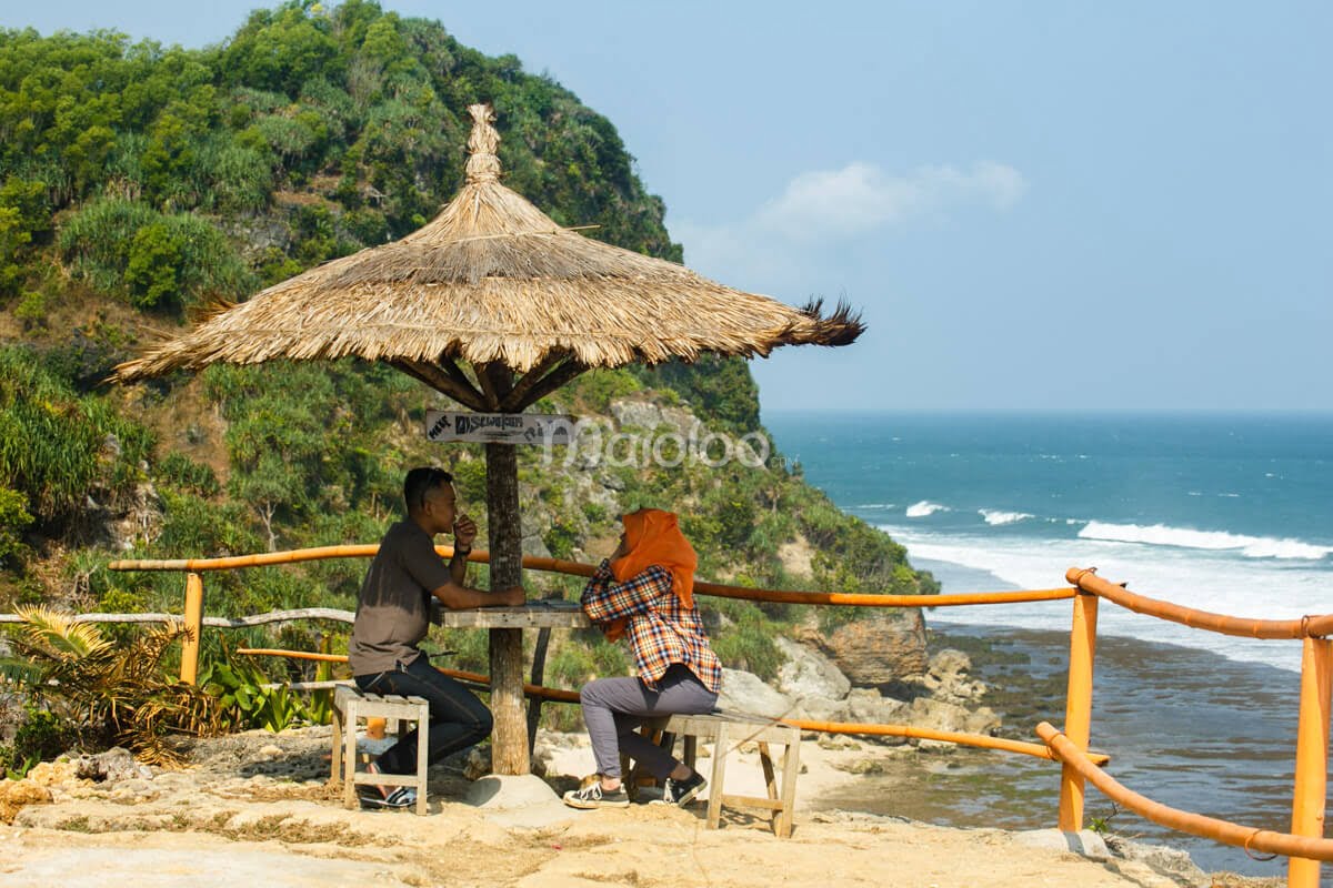 A gazebo on a cliff overlooking Pok Tunggal Beach with a man and woman seated under it.
