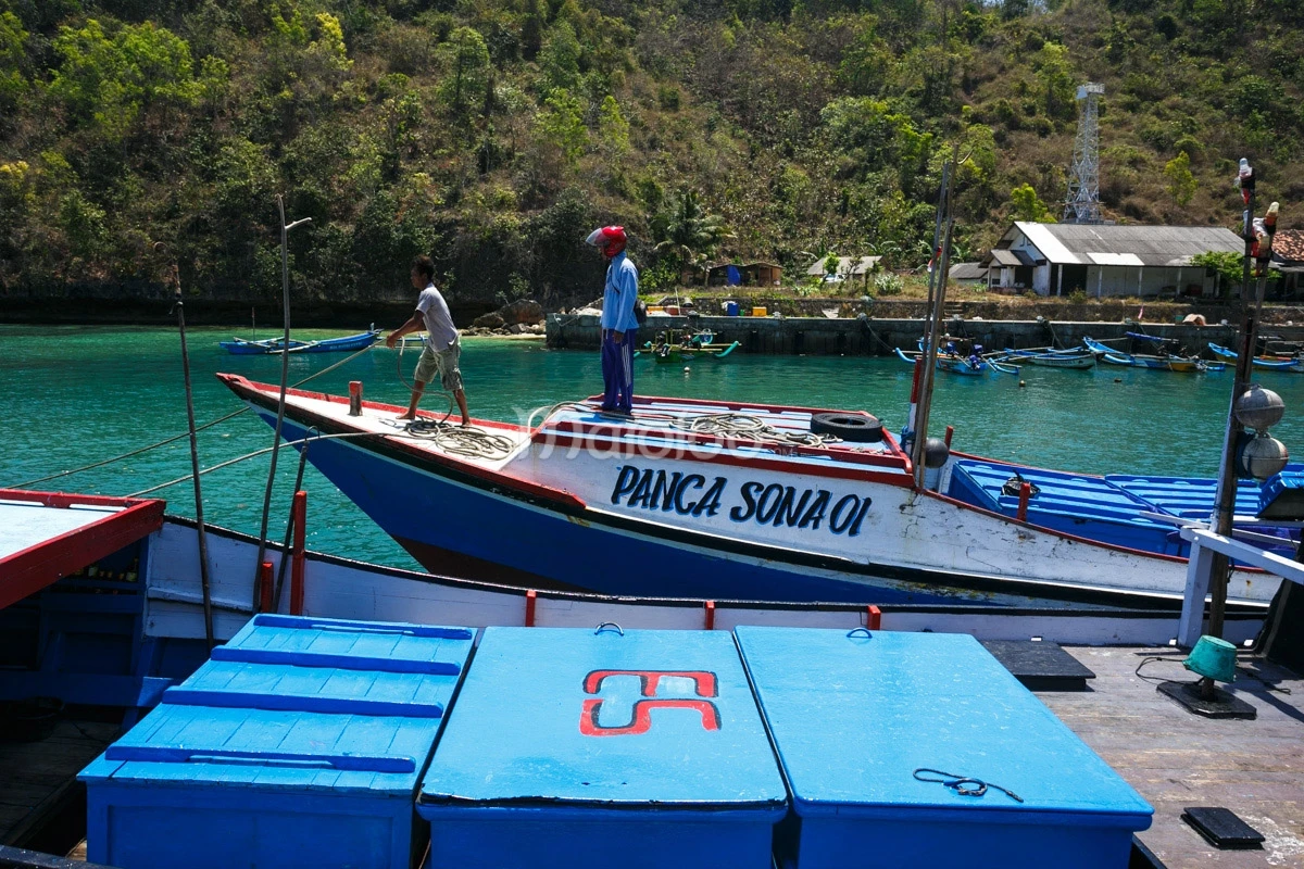 Two fishermen standing on a fishing boat at Sadeng Beach Port.