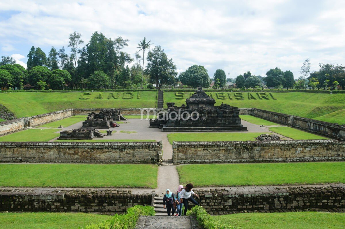 Visitors walking up the steps from Sambisari Temple located in a green pit with surrounding walls.