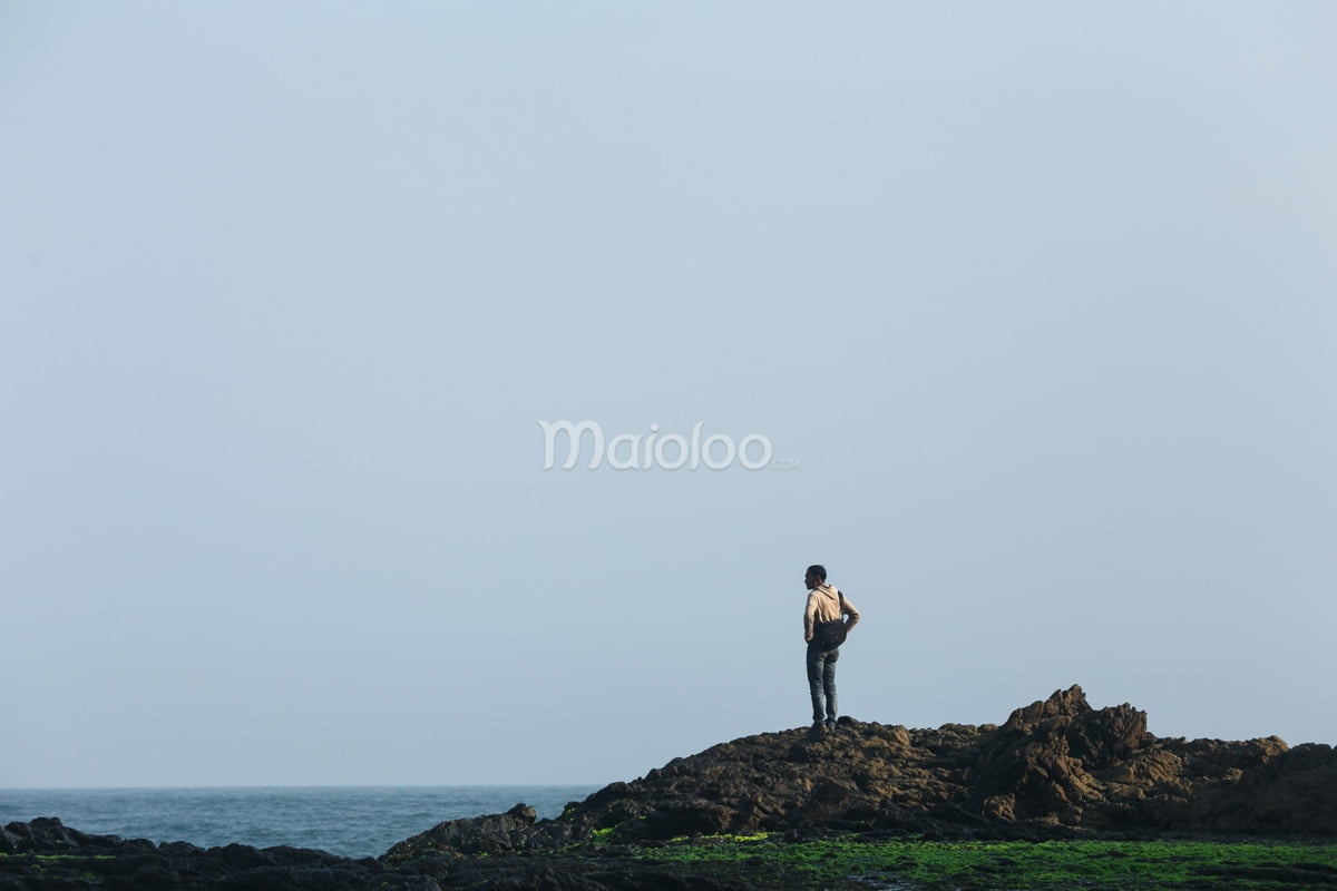 A tourist standing on a small hill at Jungwok Beach, gazing at the open sea.
