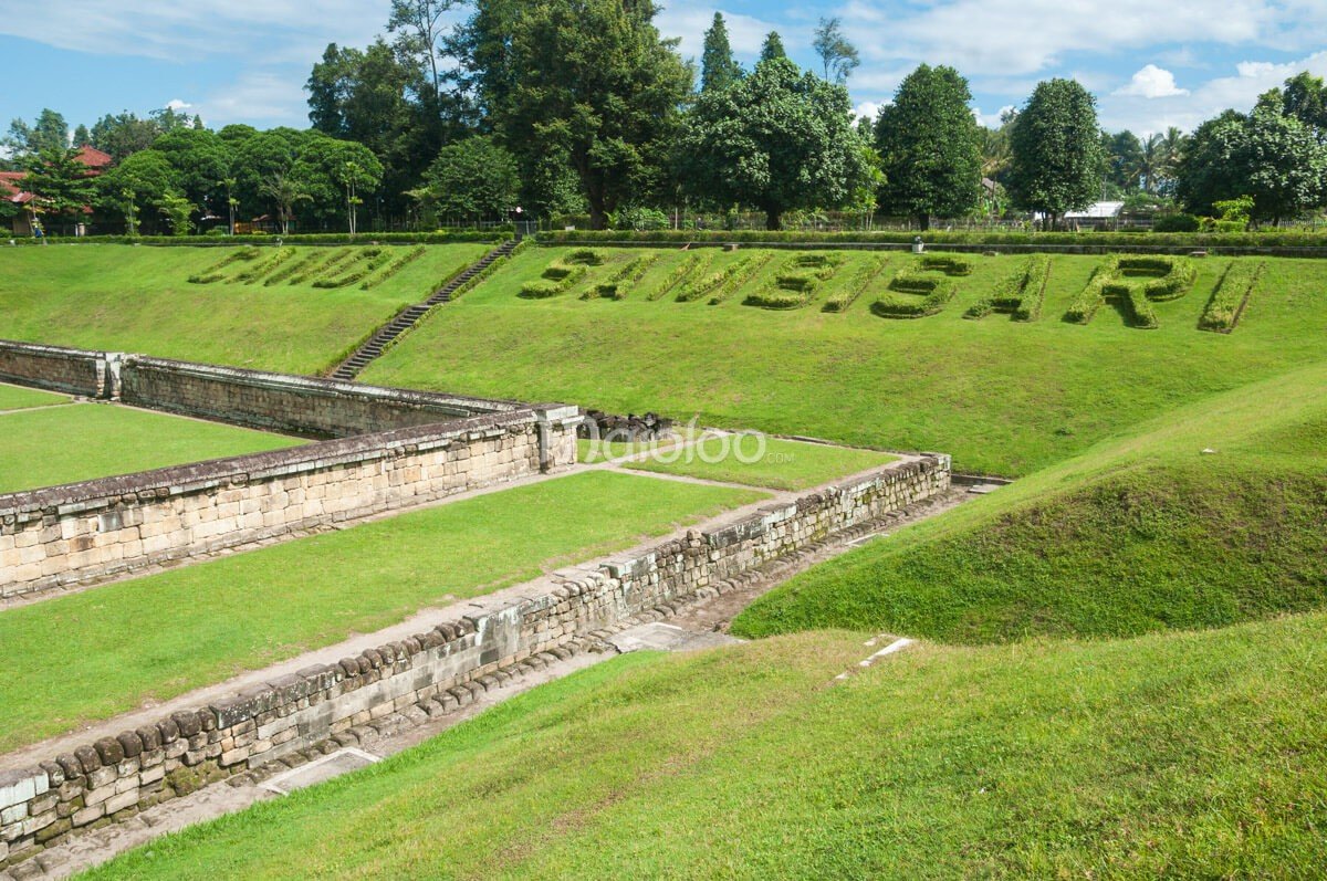 Sambisari Temple with its surrounding green terraces and stone walls under a clear sky.