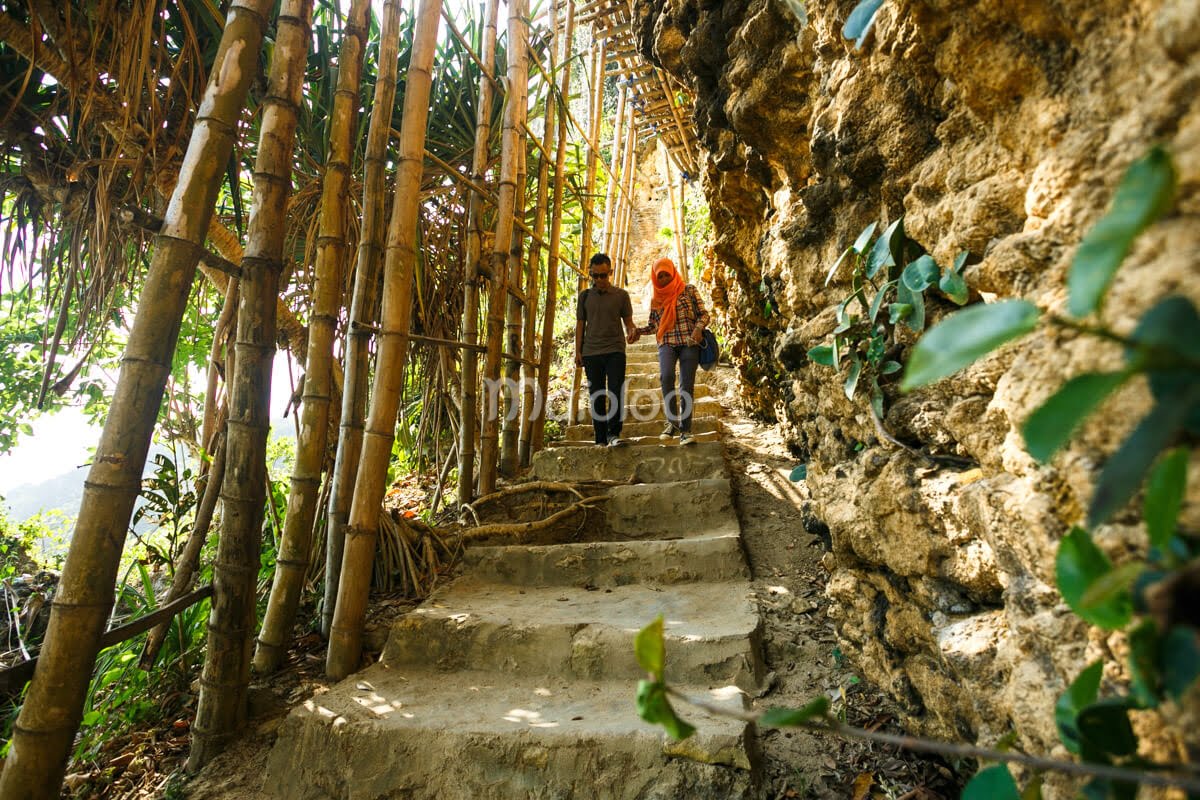 A man and a woman walking up steps along a bamboo path to the top of the cliff at Pok Tunggal Beach.