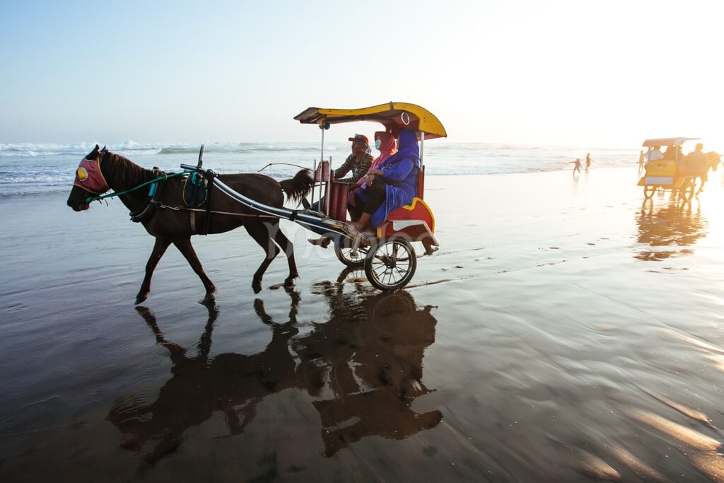 A traditional horse-drawn carriage (bendi) on Parangtritis Beach with people enjoying the ride.