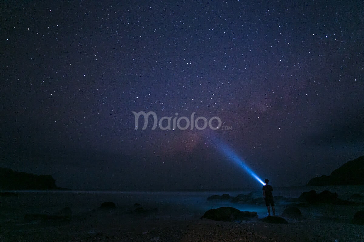A person shining a flashlight towards the Milky Way at Wediombo Beach, Yogyakarta.