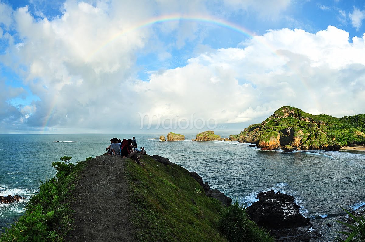 Visitors enjoying a morning view with a rainbow at Siung Beach.