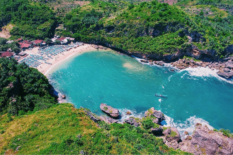 Aerial view of Ngrenehan Beach with turquoise water and surrounding green cliffs.