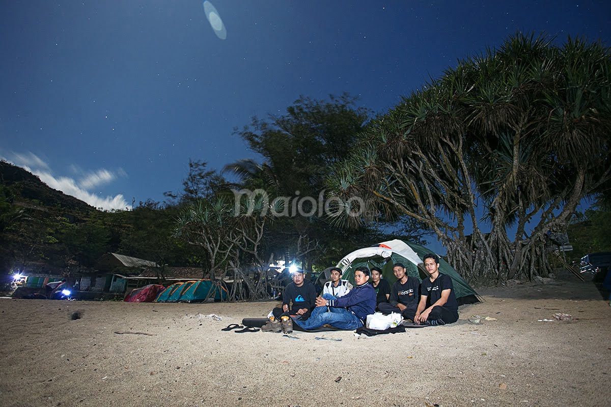 A group of people camping on the beach at night, sitting in front of a tent at Siung Beach.