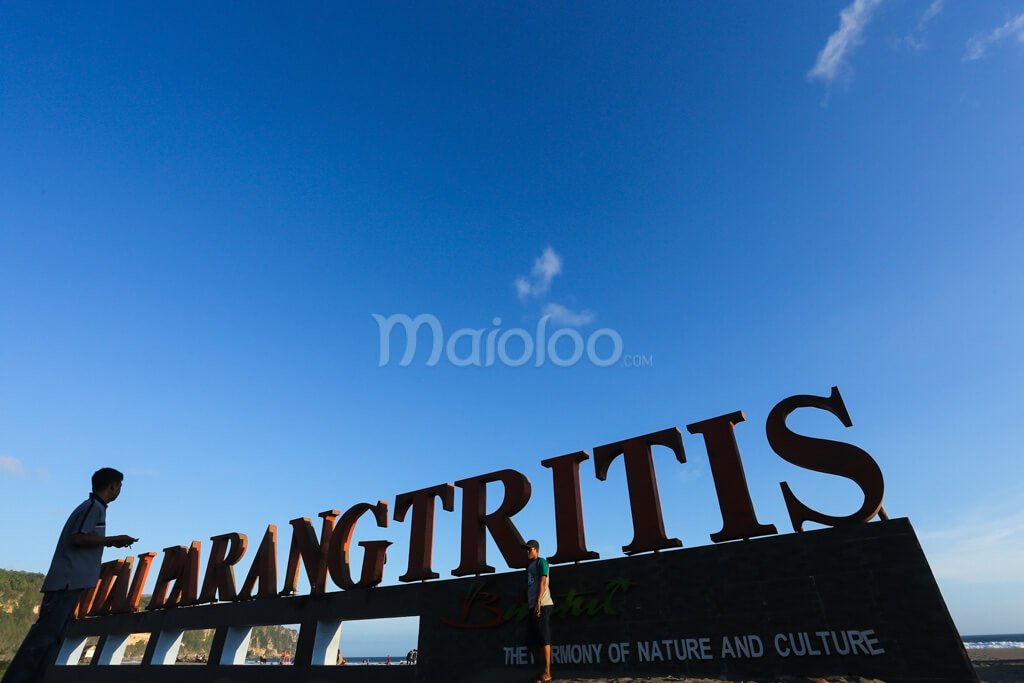Visitors taking photos in front of the Parangtritis Beach landmark sign.