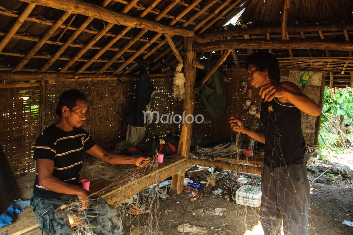 Two men preparing fishing nets inside a bamboo hut.