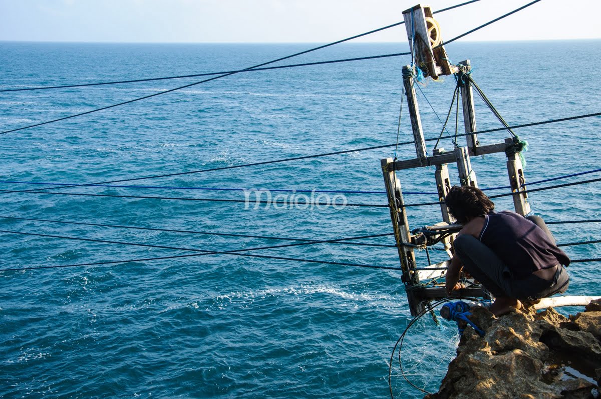 A man preparing a gondola at the edge of a cliff with the ocean in the background.