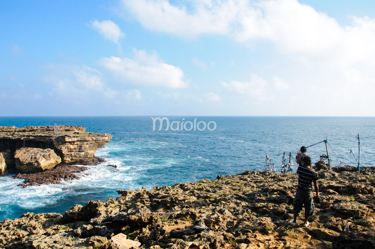 Two men standing on the rocky cliffs at Timang Beach with the ocean in the background.