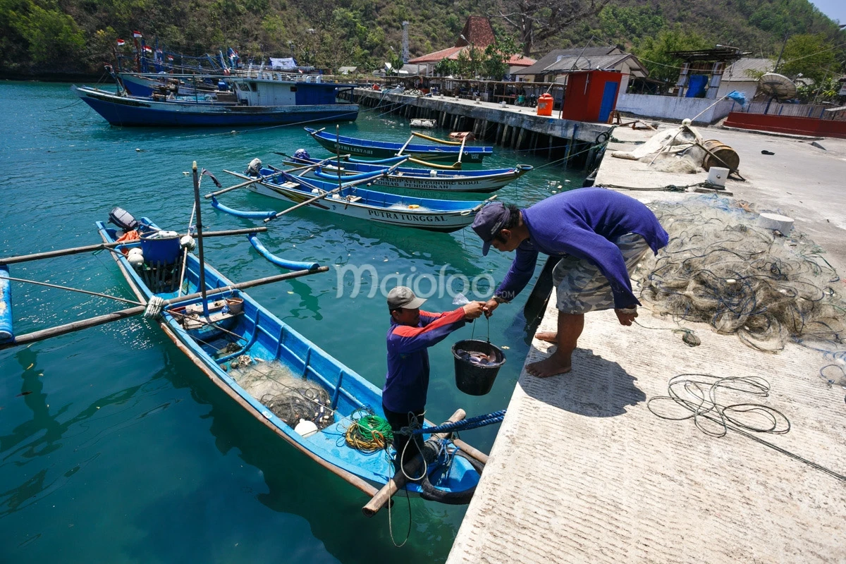 Two fishermen at Sadeng Beach preparing nets and bait on the dock before heading out to sea.