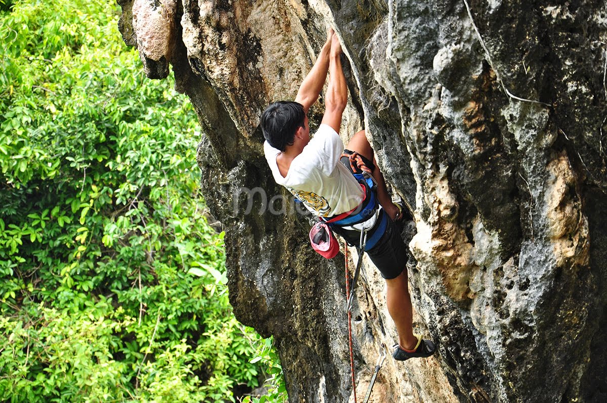 A climber grips the rocky surface while ascending a cliff at Siung Beach.