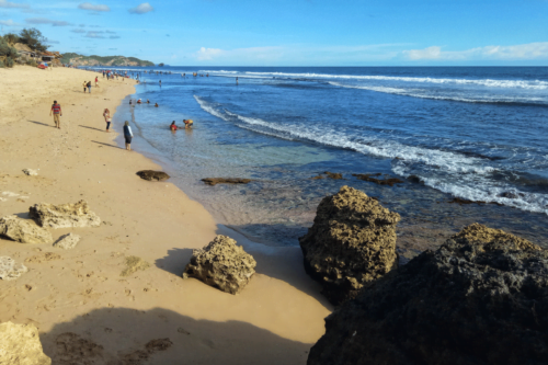 People enjoying the long stretch of white sand and gentle waves at Sepanjang Beach.