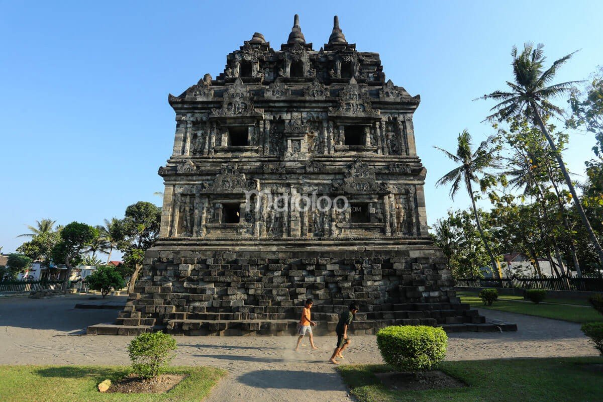 Side view of Sari Temple with two children walking by.