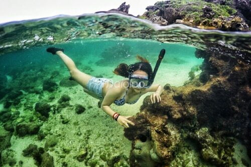 A tourist snorkeling underwater at Nglambor Beach, surrounded by clear turquoise water and rocky underwater scenery.