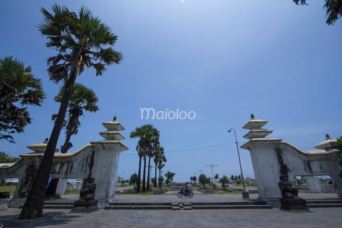 The south gate of Cepuri complex at Parangkusumo Beach with statues and palm trees under a clear blue sky.