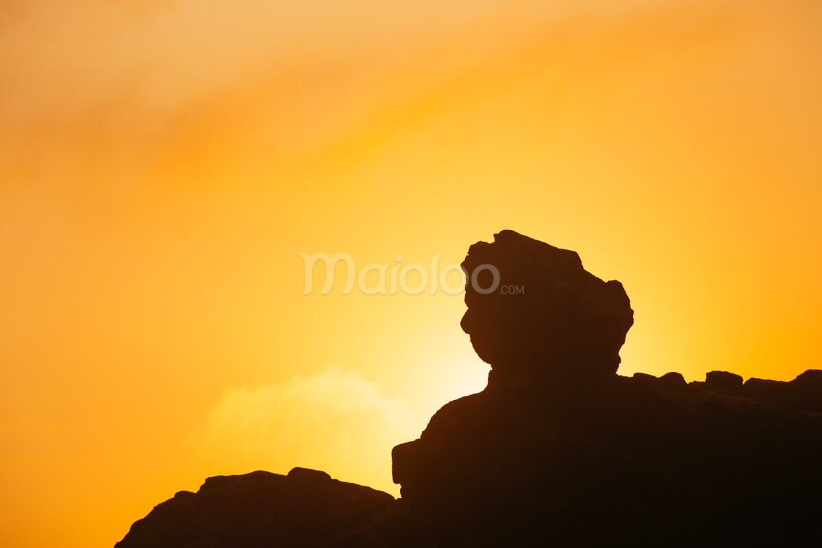 Silhouette of a rock resembling a face or sphinx at Wediombo Beach during sunset.