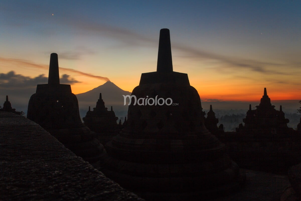 Silhouette of Borobudur Temple's stupas at sunrise with Mount Merapi in the background.
