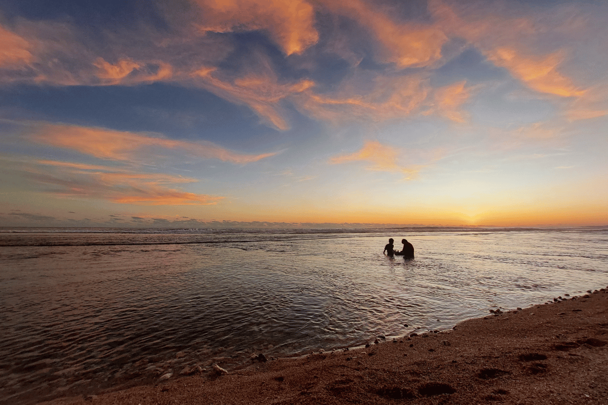 Two people enjoying the calm waters at Sepanjang Beach during a beautiful sunset.