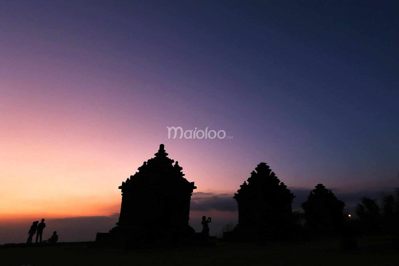 Silhouettes of people and ancient temples at Candi Ijo during sunset.