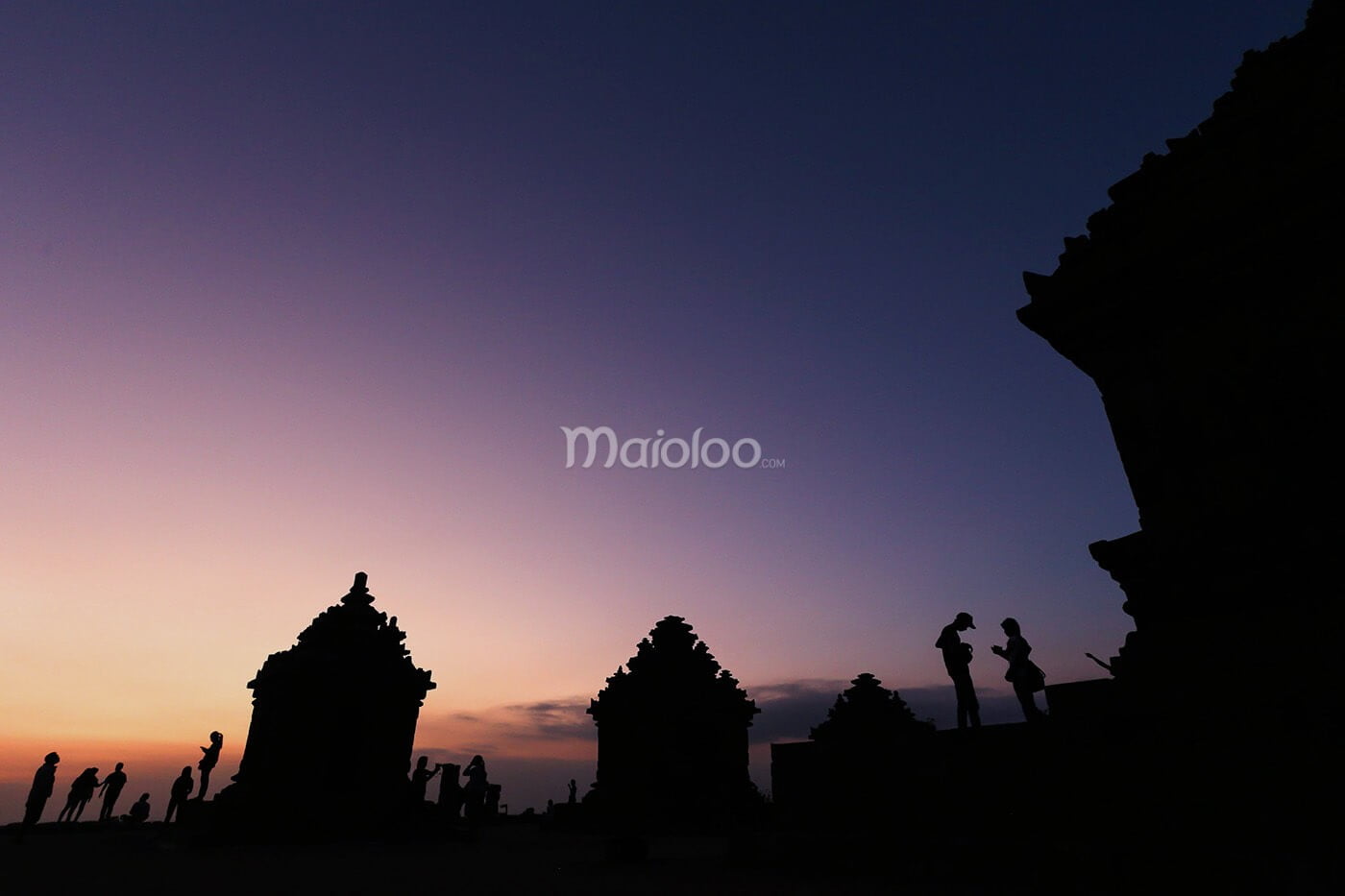 Silhouettes of people and ancient temples at Ijo Temple during sunset.