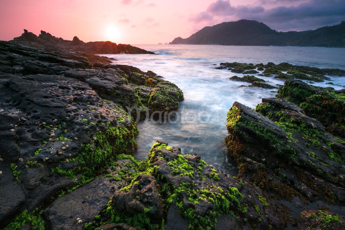 A beautiful sunset over the moss-covered andesite rocks at Wediombo Beach, Yogyakarta.
