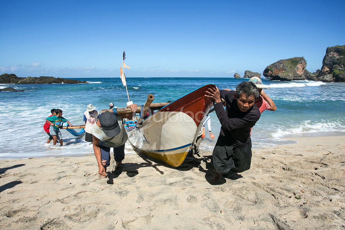 Fishermen at Siung Beach work together to push a boat ashore after a day at sea.