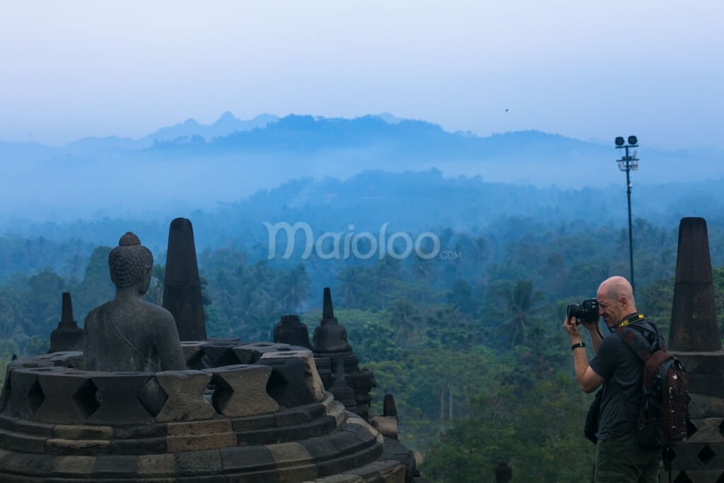 A tourist photographing an open Buddha statue at Borobudur Temple.