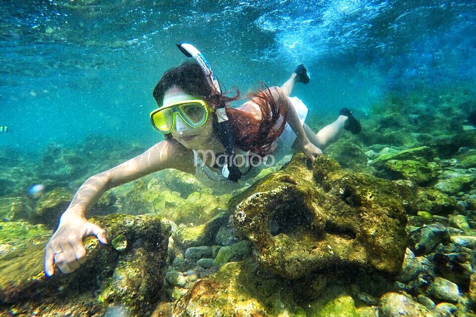 A tourist snorkeling underwater at Nglambor Beach, surrounded by clear turquoise water and rocky underwater scenery.