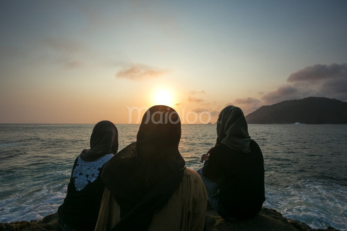 Three women in hijabs watching the sunset at Wediombo Beach, Yogyakarta.