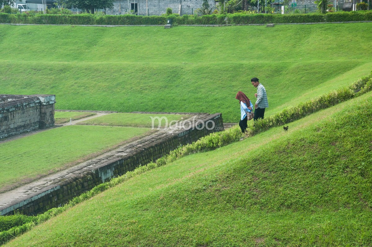 Two visitors walking down the grassy steps at Sambisari Temple.