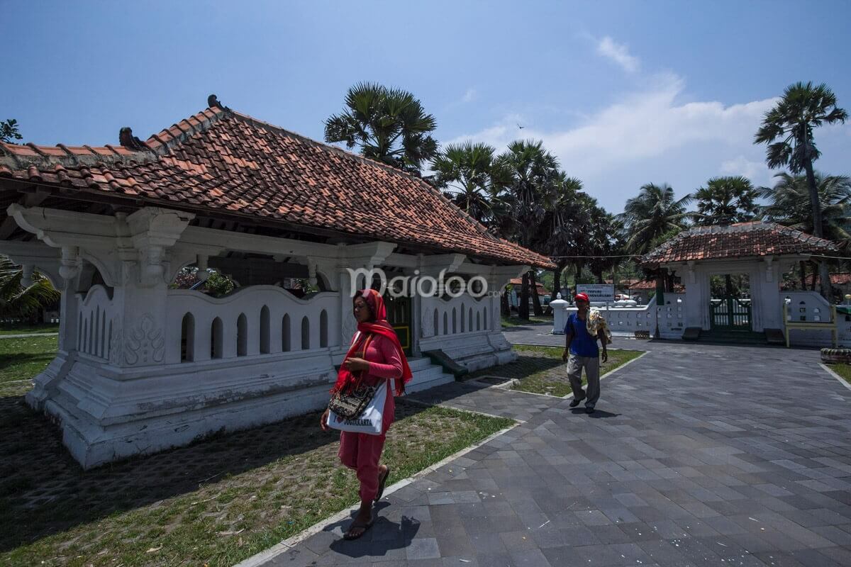 Two visitors walking at the Cepuri Parangkusumo complex, with traditional Javanese buildings in the background.