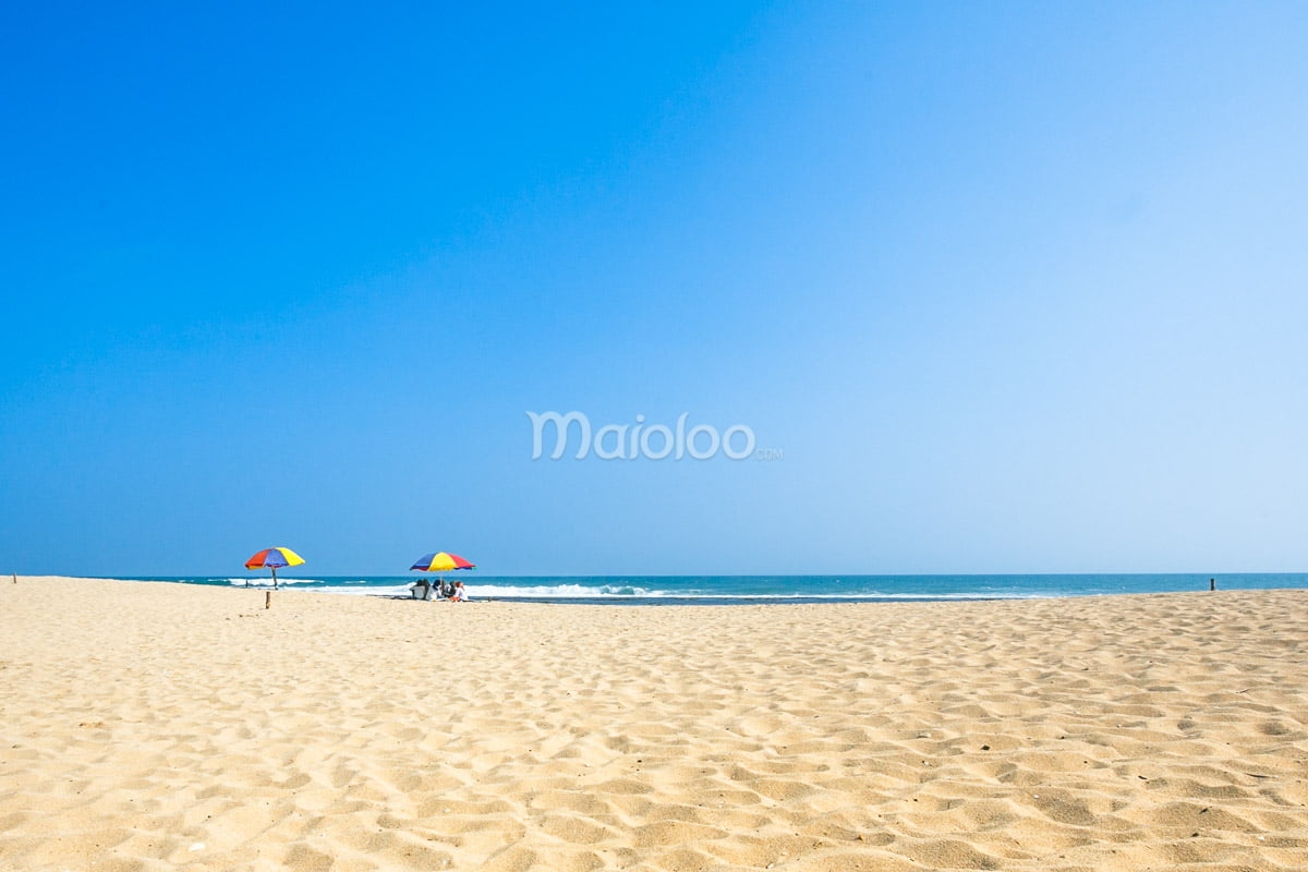A stretch of white sand at Pok Tunggal Beach with two colorful umbrellas and the blue sea in the background.