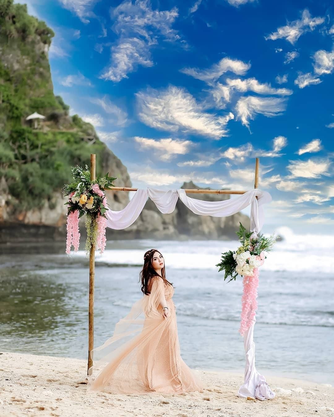 Woman in a flowing dress posing under a decorated arch on Nguyahan Beach.