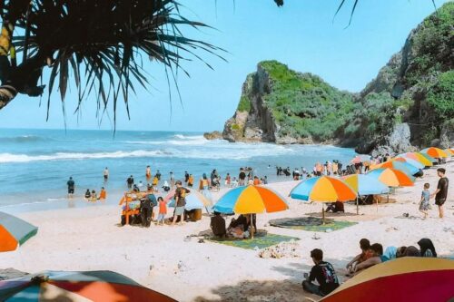 People enjoying a sunny day at Nguyahan Beach with colorful umbrellas.