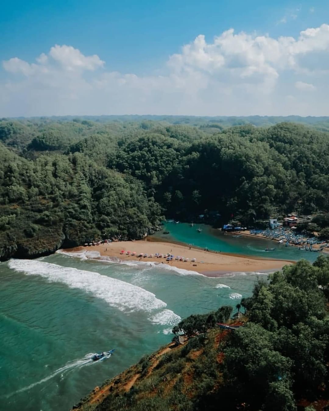 Aerial view of Baron Beach with turquoise water, sandy shore, and lush green hills under a clear blue sky.