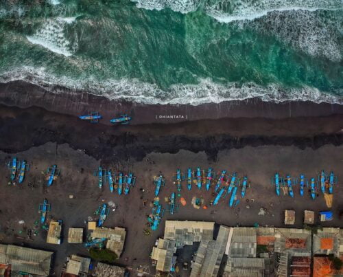 Aerial view of fishing boats and shelters on the shore of Depok Beach.