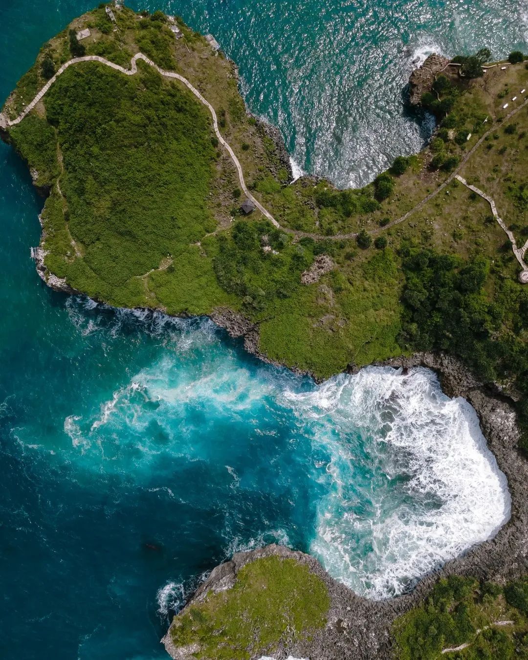 Aerial view of Kesirat Beach with rocky cliffs and turquoise waves crashing against the shore.