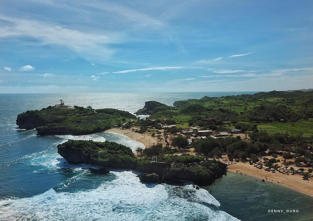 Aerial view of Krakal Beach with the yellow fish statue and the surrounding coastline and hills.