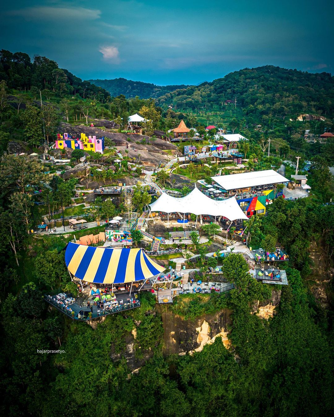 An aerial view of Obelix Hills with colorful buildings, striped tents, and lush green surroundings.