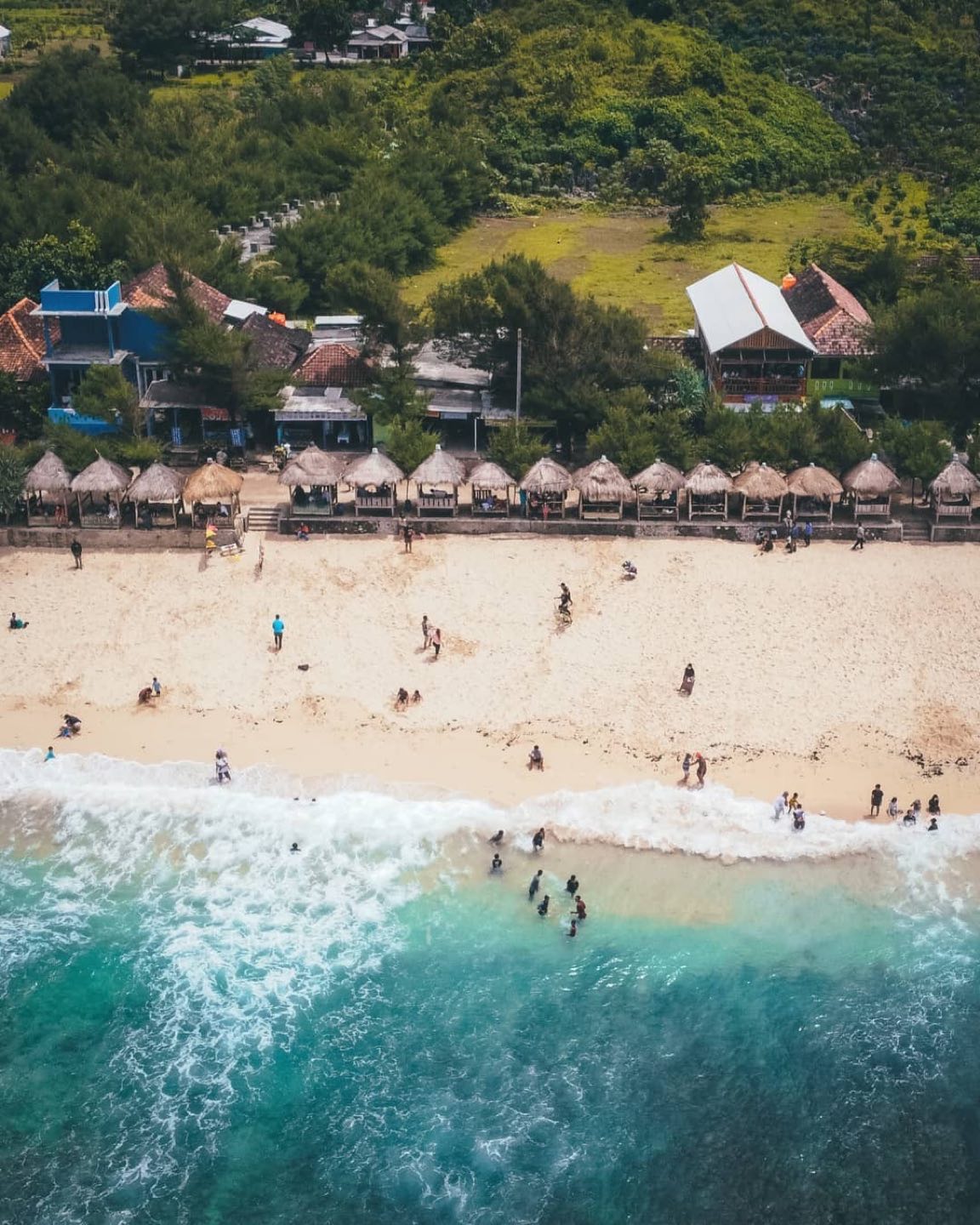 Aerial view of Slili Beach showing people relaxing on the sand and swimming in the clear blue water.