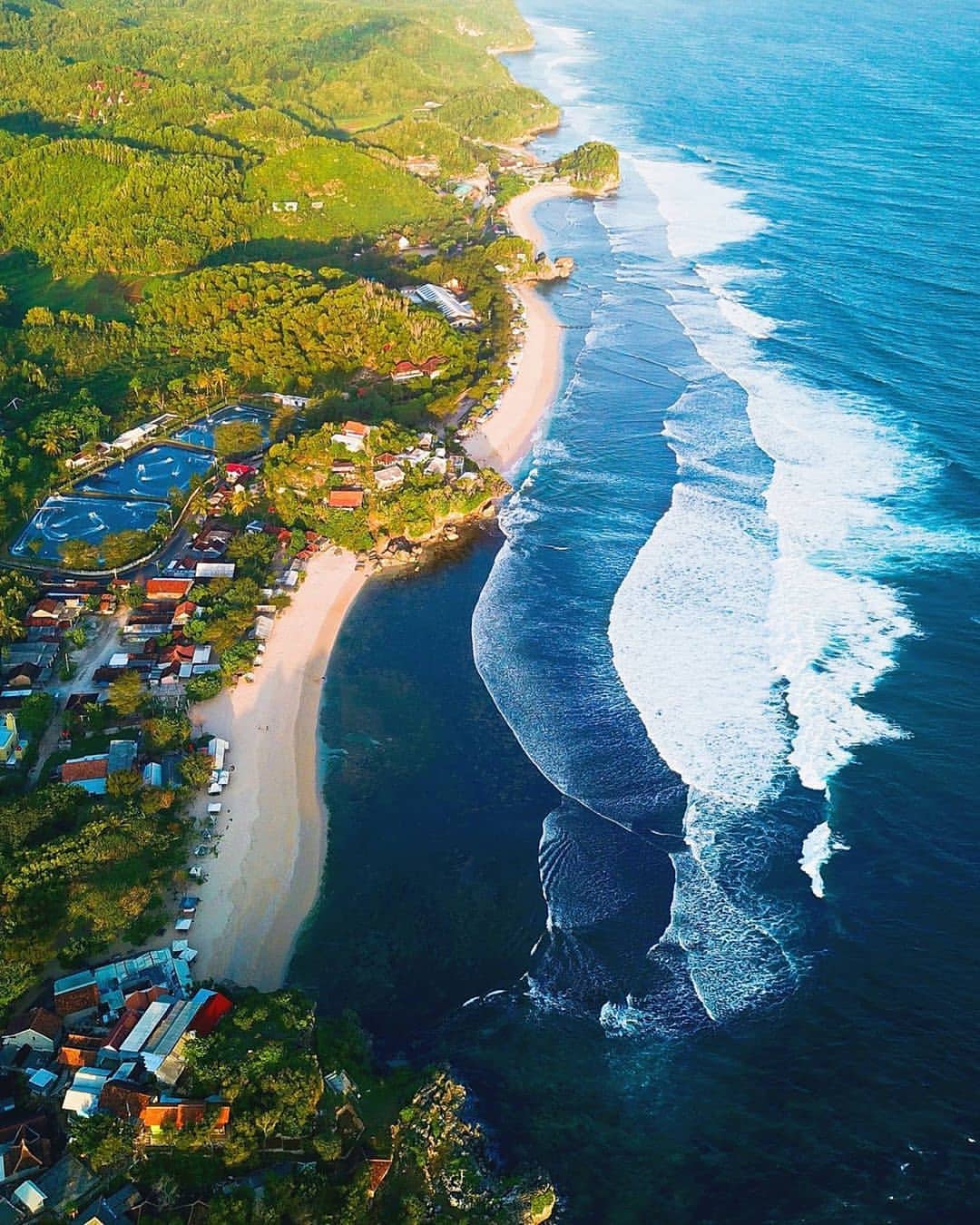 Aerial view of Sundak Beach with clear blue waters, white sandy shore, and surrounding lush greenery.