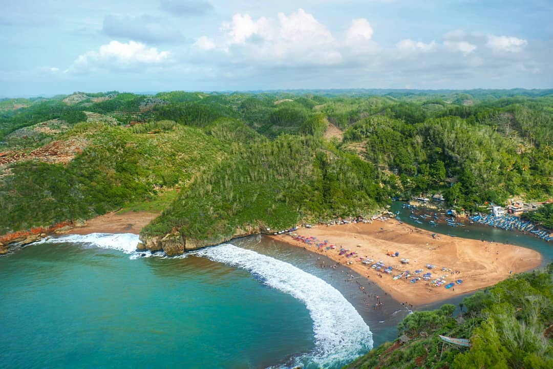 Aerial view of Baron Beach with a turquoise sea, sandy shore, and surrounding green hills.