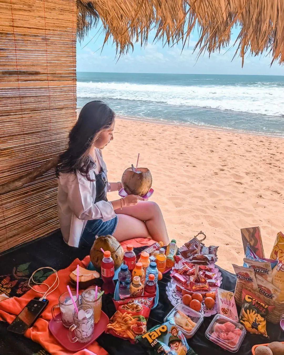 Girl enjoying a picnic with snacks and drinks at Watulawang Beach.